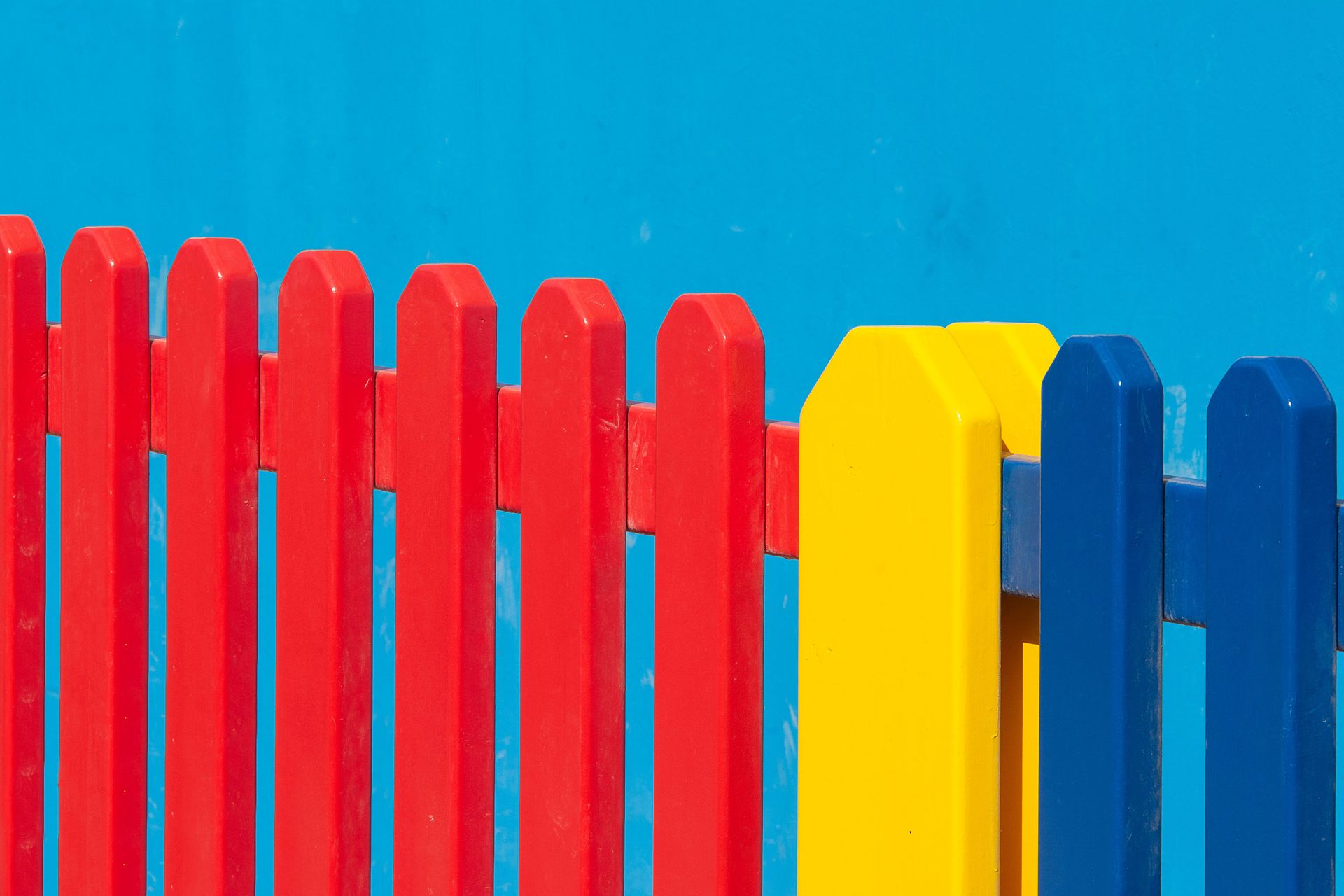 Vibrant red, yellow, and blue wooden fence panels against a clear blue backdrop.